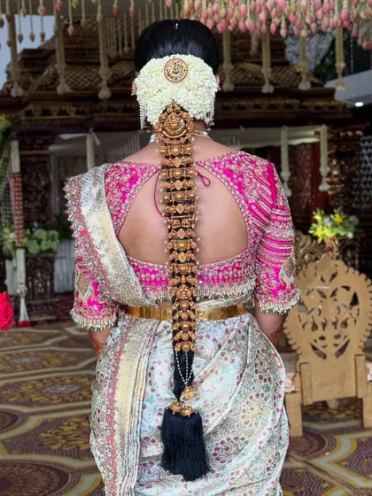 This is a grand Muhurtham bridal look, featuring a full Jada Billai set on a thick, dark braid. The style is completed with a large jasmine veni, creating a truly regal and traditional South Indian bridal statement.
