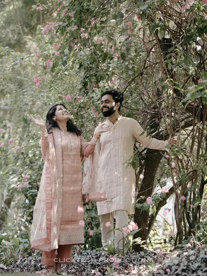 A joyful shot of a couple in a garden, looking up as flower petals fall around them, capturing a magical, romantic moment.