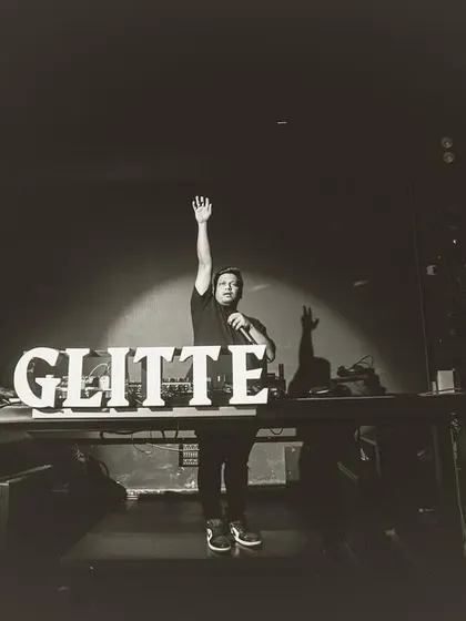 Standing on the stage at Glitte, taking a moment to connect with the crowd. The spotlight and the club's branding create a powerful image.