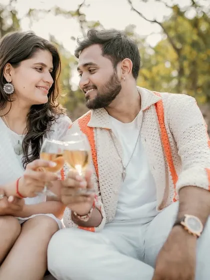 A toast to their future together. The couple clinks glasses during their romantic beach picnic, smiling at each other in a moment of shared happiness.