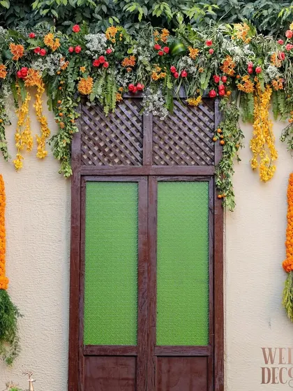 A close-up of the heritage-style door and window backdrop, adorned with fresh marigold garlands and cascading florals. This element was key to creating the 'Old Delhi' architectural feel.