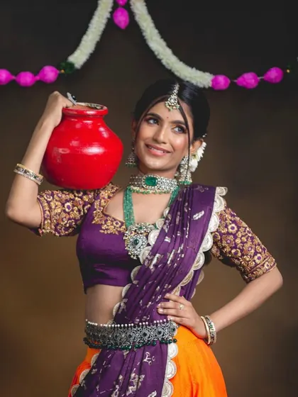 A playful shot of the model holding a pot, looking like a traditional village belle. The emerald jewellery adds a touch of royalty to the rustic charm.