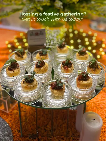 A tray of our savory bites, elegantly arranged on a mirrored stand with soft, festive lights in the background. The text overlay provides a clear call to action for potential clients hosting a gathering.