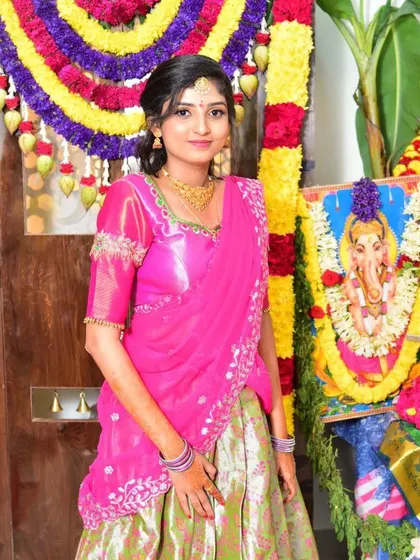 This client looks lovely in a half-saree ensemble for a traditional function. The bright pink blouse and dupatta feature delicate gold embroidery that complements the light green skirt.