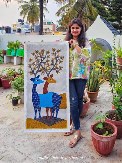 Me holding the completed Gond deer painting. This gives a sense of the artwork's size and how it can be a significant feature piece on a wall.