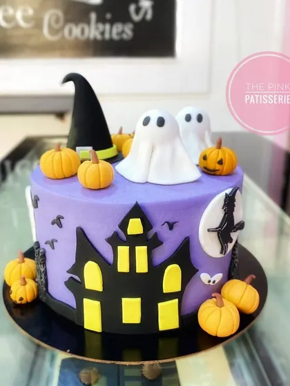 A spooky and fun Halloween cake. This purple cake is decorated with a haunted house silhouette, fondant ghosts, pumpkins, and a witch's hat.