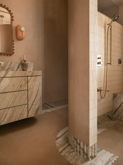 The master bathroom at Soft Serve is a 'chic desert dream,' bathed in blush-toned micro-concrete. A monolithic vanity in veined Corteccia marble appears to float against the wall.
