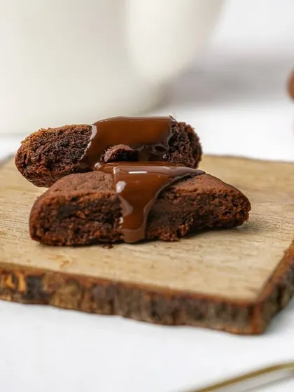A soft chocolate cookie broken in half with chocolate sauce drizzled on top, emphasizing its gooey texture.