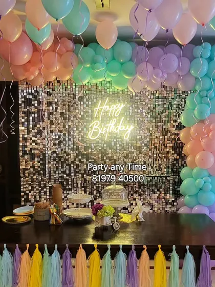 A pastel-themed decoration over a dining table, featuring a shimmer wall, balloon garland, and colorful tassels.