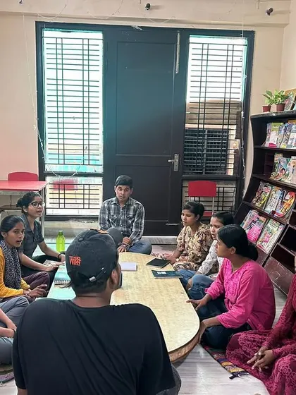 Kalakaar fellows lead a session at a community center, sitting with students around a table. This informal setting encourages open conversation and collaborative learning.