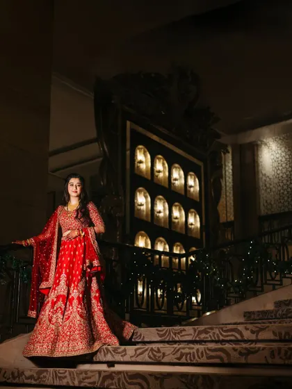 A grand bridal portrait on the iconic staircase of the St. Regis Mumbai. The bride's red lehenga stands out beautifully against the dramatic, luxurious backdrop.