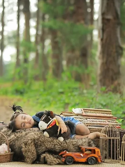 A one-year-old girl takes a nap amidst vintage props during her outdoor photoshoot in a serene, wooded area.