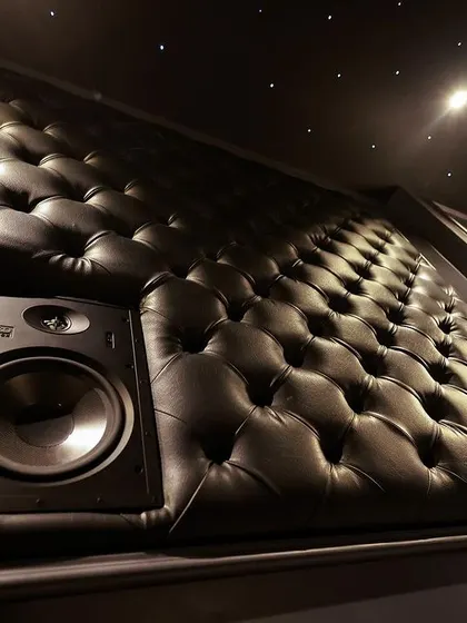 A close-up of an OSD Black series in-wall speaker seamlessly integrated into a custom black leather tufted acoustic panel. This is where high-performance audio meets luxury design.