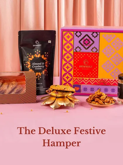 The Deluxe Festive Hamper offers a wonderful variety of our bestsellers. It includes our Almond & Cranberry Granola, assorted cookies, and a jar of Spiced Peri-Peri Cashews, all packed in a colorful and festive gift box.
