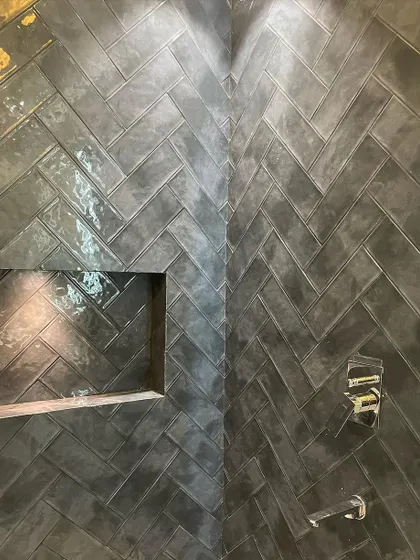 A detailed look at the glossy, handmade-look tiles in the shower. The chevron pattern adds a dynamic and modern feel, while the dark color creates a cozy, enveloping atmosphere.