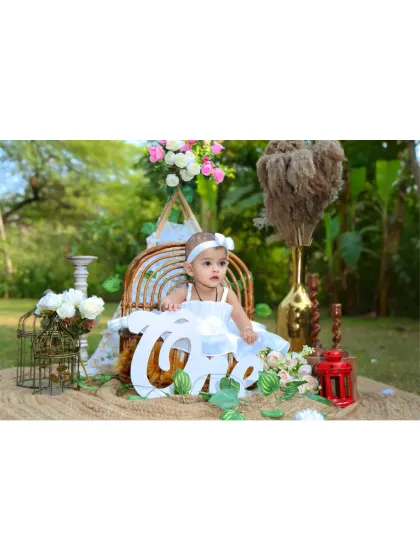 The birthday girl in her fairy costume, posing with a 'One' sign in a beautifully decorated outdoor setup.