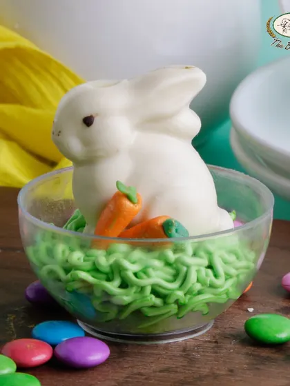 A close-up of our 'Bunny in a Globe' creation. The detailed white chocolate bunny, complete with tiny carrots, sits in a clear cup, making it a perfect individual dessert for Easter.