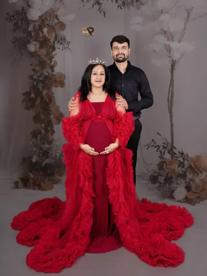 A royal couple portrait. The mom-to-be wears a crown and a magnificent red gown, standing proudly with her partner. This is a wonderful way to capture your journey into parenthood together.