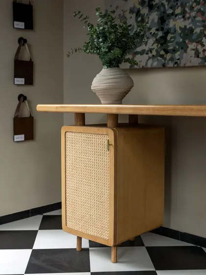 A detail of a custom-designed desk with a light oak finish and a cane-fronted cabinet. The clean lines and natural materials make it a beautiful and functional piece for a home office.