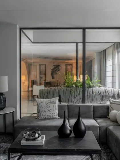 Glass partitions and an open layout create a sense of flow in this living area. A plush sectional sofa is arranged around a central planter, bringing a touch of nature indoors.