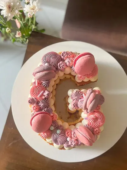 Letter cakes are a fun and personal way to celebrate. This 'G' monogram cake is decorated with beautiful monochrome buttercream swirls in shades of pink and purple, topped with matching macarons.