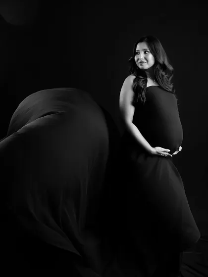 A powerful black and white portrait. The flowing fabric and dramatic lighting create a timeless and artistic image that celebrates the beauty of the female form during pregnancy.