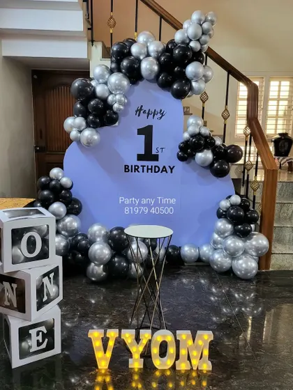 A modern and stylish first birthday setup in black, silver, and lavender. It includes a custom backdrop, "ONE" letter blocks, and light-up marquee letters.