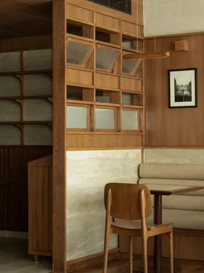 Seating nooks at QBF Coffee, where I used built-in banquettes and travertine wall panels to create comfortable, intimate zones. The large windows connect these serene interiors with the greenery outside.