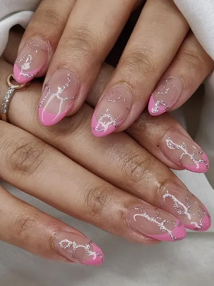 A creative design on almond nails, featuring a pink French tip on a sheer base with delicate, sparkling silver swirls.