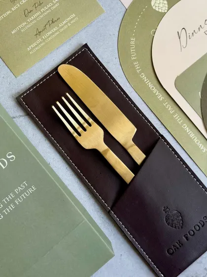 A close-up of the custom-branded cutlery set for the Oak Foods event. The gold fork and knife are presented in a handsome leather sleeve embossed with the company logo.