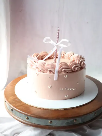 A minimalist dusty pink cake with delicate piping on top and a single candle tied with a bow.