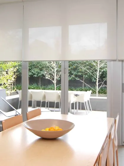 Another shot of the white roller blinds in a dining area, proving their versatility and clean finish for modern homes.