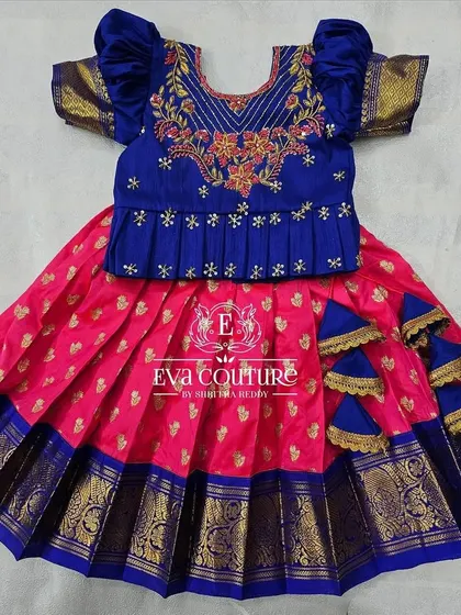 A flat-lay view of the blue and pink baby lehenga, showing the puff sleeves and embroidered details on the top.