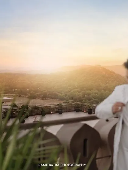 The groom gets ready on a balcony overlooking the Aravalli hills at sunset, a quiet moment of anticipation.