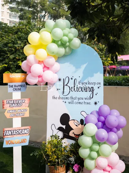 A whimsical welcome sign for a Disneyland-themed Christmas brunch, featuring Mickey Mouse and pastel balloon clusters.