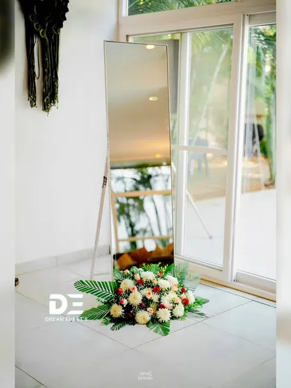 A simple and elegant detail for a Haldi event. A standing mirror is tastefully decorated with a fresh flower arrangement at its base, adding a touch of sophistication to the decor.