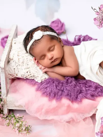 A beautiful newborn portrait featuring a baby sleeping on a miniature bed adorned with purple and pink flowers. The soft fabrics and floral elements create a gentle and feminine look.