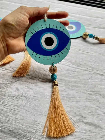 A close-up of the Evil Eye hanging, showing the hand-painted details and the decorative beads.