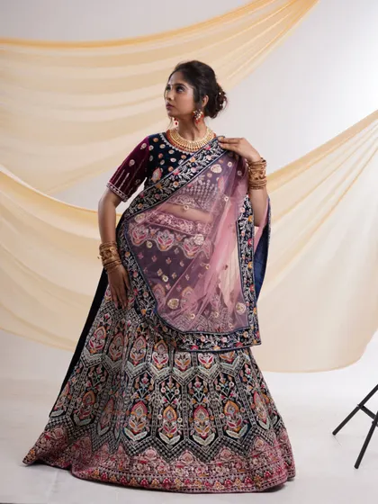 A side profile of the navy blue velvet lehenga, displaying the full, voluminous skirt and the elegant drape of the sheer pink dupatta.
