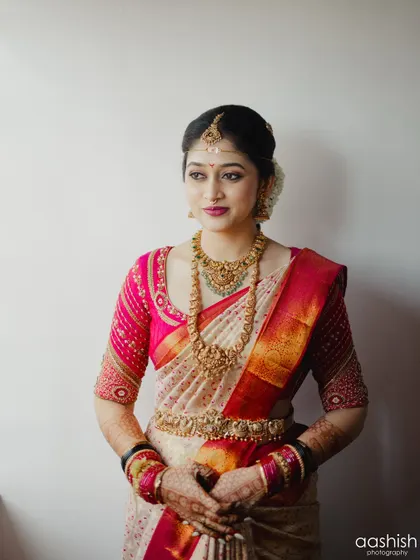A classic bridal portrait. The makeup features a beautiful berry-toned lip and defined eyes, perfectly complementing her pink and gold silk saree.