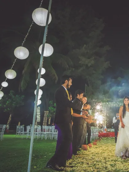 The bride makes her entrance at a beautiful outdoor reception, with guests holding sparklers. The warm lights and happy faces create a magical atmosphere.