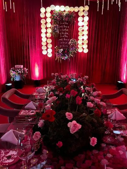 A dramatic, red-themed tablescape with Japanese-inspired elements. The centerpiece of moss and roses sits on a mirrored table, reflecting the moody lighting and creating an atmosphere of intense romance and sophistication.