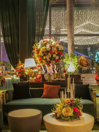 A duplicate of image 6, showing a comfortable lounge area with deep green velvet sofas and vibrant floral displays, set against a backdrop of fairy lights.