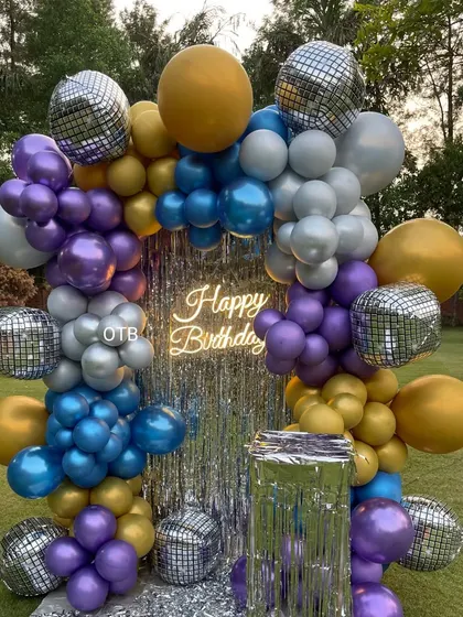A closer look at the vibrant outdoor disco-themed balloon arrangement in purple, blue, silver, and gold.