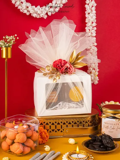 A premium white Diwali hamper wrapped in tulle, styled against a bold red background with golden accents for a sophisticated look.