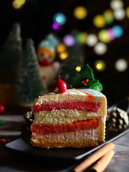 A beautifully composed shot of the rainbow pastry slice against a dark background with colorful bokeh lights. This image highlights the vibrant layers of the cake and the festive atmosphere.
