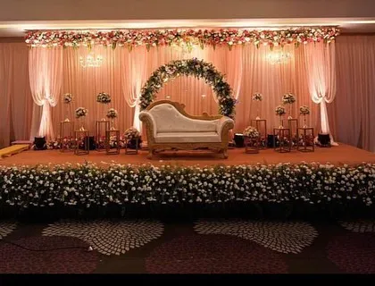 A wide view of a classic floral reception stage. The design includes a central floral arch for the couple's seating and a stage front lined with dense flowers, creating a lush and romantic atmosphere.