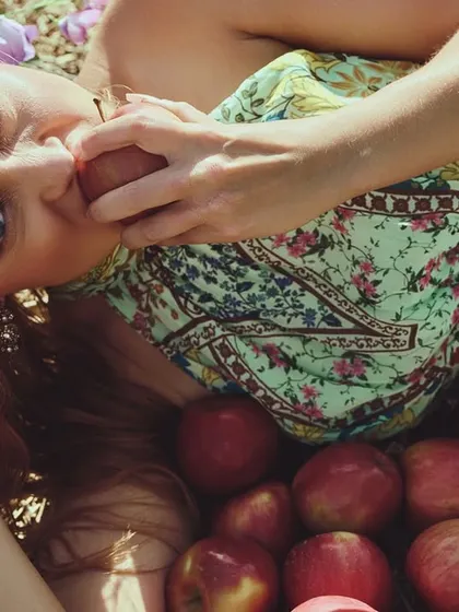 A surreal take on natural beauty. The model is surrounded by a sea of apples, creating a dreamlike, almost biblical scene with warm, golden lighting.