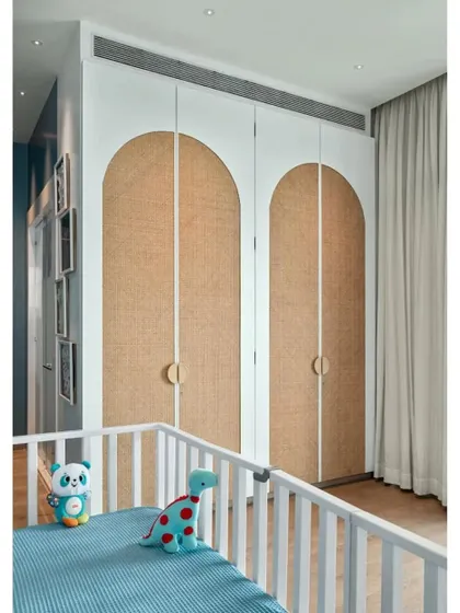 The arched wardrobe doors with cane webbing in the nursery add a touch of warmth and natural texture, balancing the cool blue tones of the room.