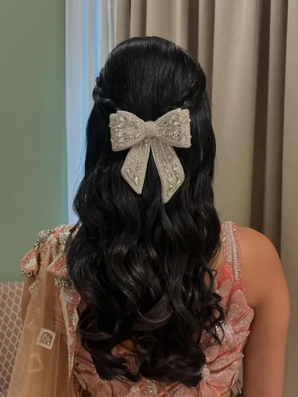 A modern and glamorous half-up style featuring an oversized, pearl-embellished bow clip.
